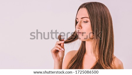 Portrait of young frustrated woman looking at dry split hair tips in her hand isolated. Beautiful sad worried woman with long unhealthy damaged hair in hand. Hair loss problem, hair care, treatment Royalty-Free Stock Photo #1725086500