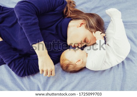 Mother kissing child lying on bed. Top view of happy young mother and adorable infant daughter lying together on bed. Family concept