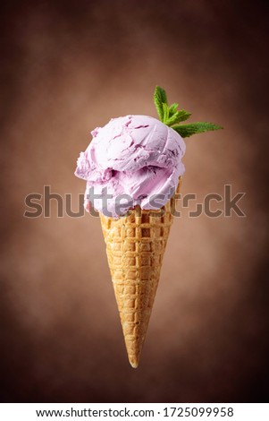 Blueberry ice cream with mint  in waffle cone. Ice cream on a brown background.