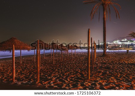Straw umbrellas on empty beach in Marbella, Spain. Night photography with stars