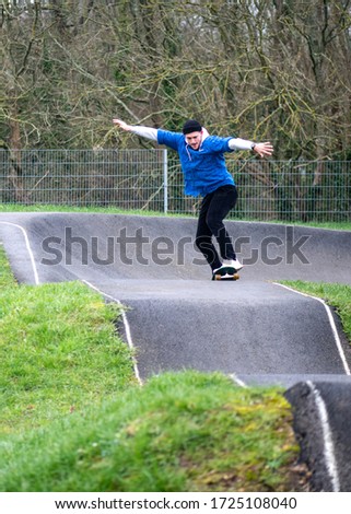Young man in sportswear riding on skateboard with arms outstretched along hilly asphalt road performing tricks in skate park in daylight