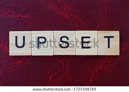  text the word upset from gray wooden small letters with black font on an red table