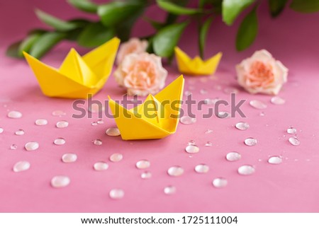 Yellow spring paper ships,boats floating in sparkling water drops on purple background.Pink full roses,branch of green leaves.Summer concept.Greeting card.DIY family activity entertainment with kids.