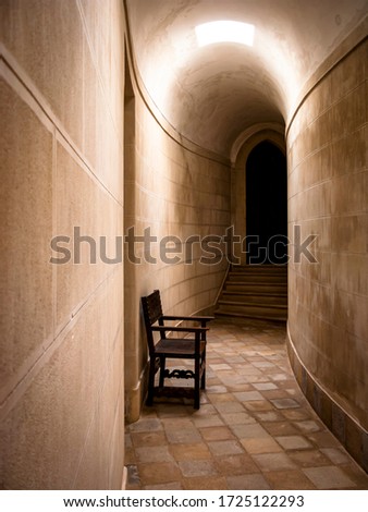 Narrow curved tunnel with a chair that ends in a staircase with a door.