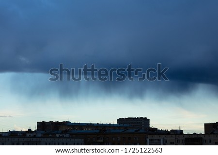 Blue/Black clouds and rain coming from above on the roofs of the city. Silhouette of the city under a thunderclouds