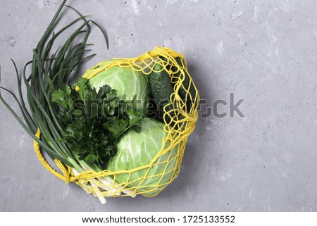 Reusable yellow mesh string bag with green vegetables on a gray concrete background. Plastic free concept, Space for text