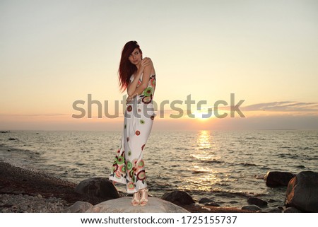 young slim girl in a dress posing at sunset on the sea