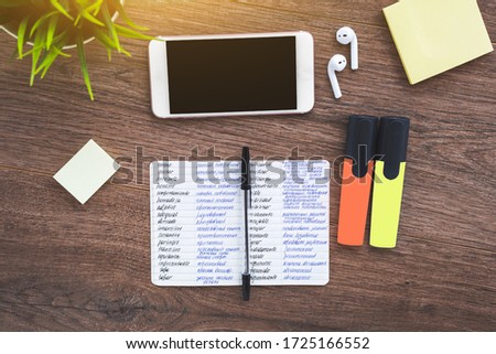 Notebook for writing foreign words dictionary, smartphone, wireless headphones on a wooden brown desktop