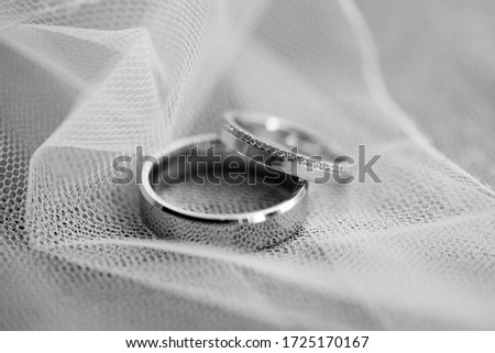 Black and white macro picture of the two new elegant gold wedding rings with diamonds placed on the white bridal veil background