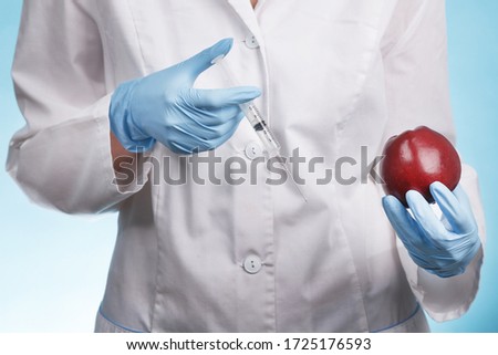 Portrait of a female doctor standing with an Apple and a syringe on a blue background. concept of enhancing the growth of vegetables and fruits