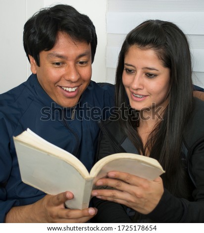 Young couple reading together a magazine in their living room at home.
