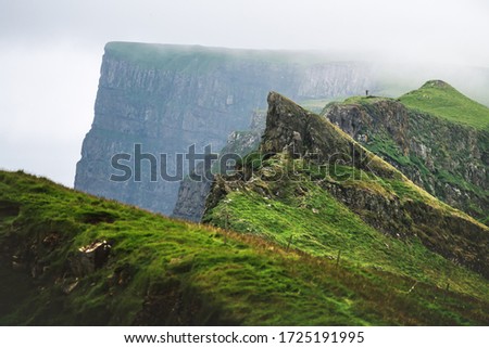 Foggy view of gorgeous mountains of Mykines island with tourist on high viewpoint. Faroe islands, Denmark. Landscape photography