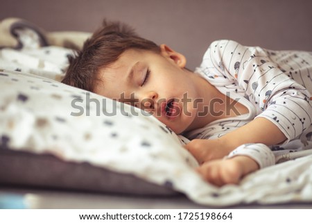 Lovely face expression with open mouth of blonde caucasian three years old child, sleeping on king bed. Sweet dreams. Little baby boy sleeping while lying on couch at home