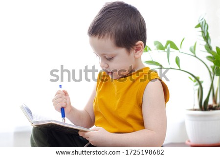 The boy draws with pencils at the table. Homework. A boy at the window with a flower. Online learning. Quarantine self-isolation. We are sitting at home. Children's entertainment with self-isolation