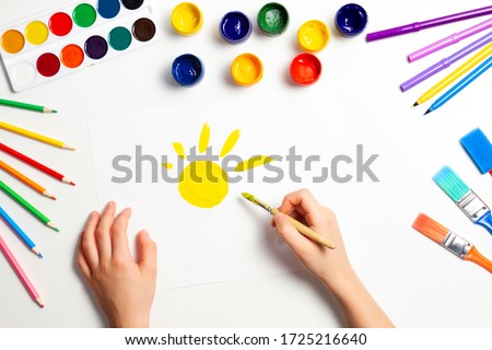 Kid hands painting yellow sun. Top view to white table with art supplies Royalty-Free Stock Photo #1725216640