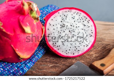 A dragon fruit cut in half next to a knife and blue cloth on a rustic wooden table.
