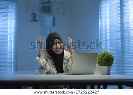 soft focus of Beautiful Asian Muslims wearing black headscarves feel stressed when working from home at night in a modern interior design workspace with the warm blue light from the windows 
