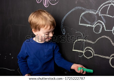 little boy draws in chalk on a slate wall of a typewriter. Close-up of European appearance. home leisure.