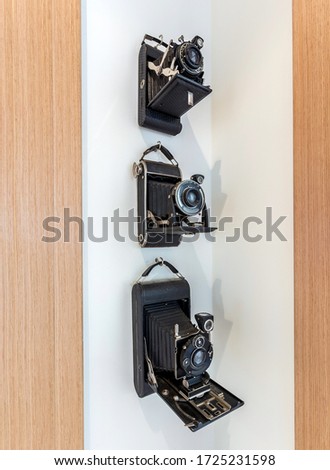Vintage cameras with a black, leather case hanging in a corner on a white wall.