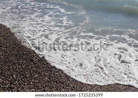 Stone pebbles, small round pebbles on the beach. Sea foam on the wolves