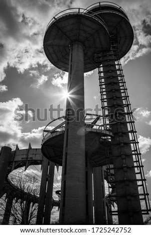 A black and white photo shows sun rays silhouetting the famous Worlds Fair observation towers of Flushing Meadows New York.