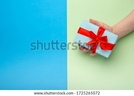 Woman holds a white gift box with a red bow on a colored background. Gift for birthday, Christmas, Valentine's Day, New year . Flat lay