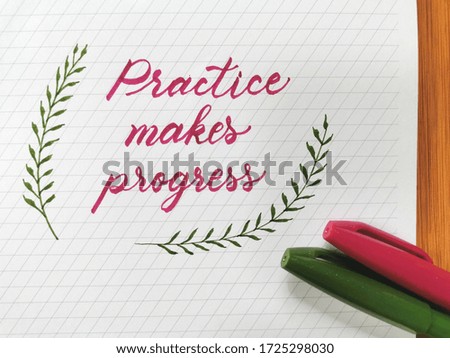 practice makes progress hand written on white calligraphy guide pad. pink lettering and green floral leaves. pink and green brush pens on paper. 