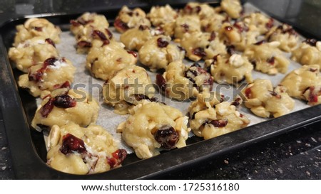 Home cooking Raw soft white chocolate chips 𝙲𝚊𝚜𝚑𝚎𝚠 and dried cranberry Cookies before baking on a cover paper on a tray.