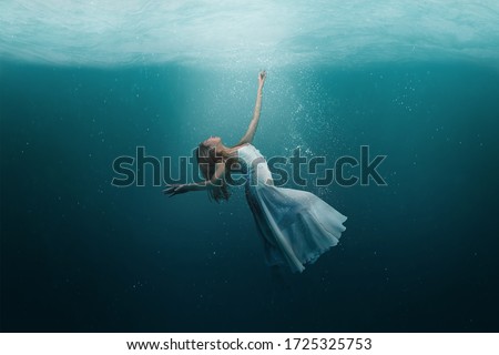 Elegant girl dancer in white dress in a state of levitation under the deep waters of the ocean with sunlight beaming on her face.  Royalty-Free Stock Photo #1725325753