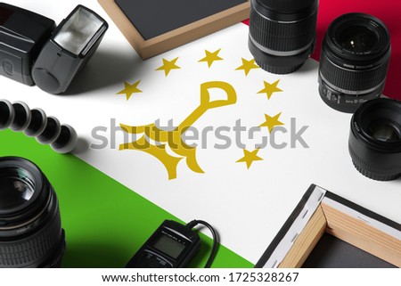 Tajikistan national flag with top view of personal photographer equipment and tools on white wooden table, copy space.