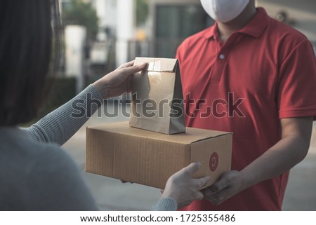Deliver man wearing face mask in red uniform handling bag and  parcel box give to female costumer Postman and express grocery delivery service during covid19. Royalty-Free Stock Photo #1725355486