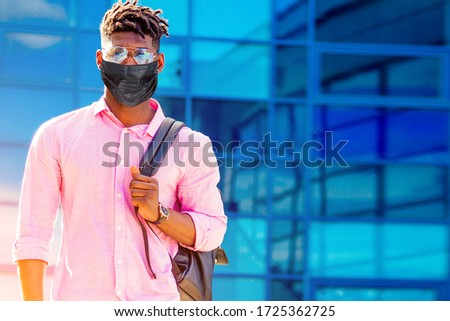 handsome trendy African American university lecturer male with glasses in stylish clothes black shirt with a backpack on the shoulders stand background of the blue windows Royalty-Free Stock Photo #1725362725