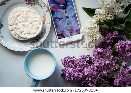 flatlay with a cup of milk, phone, rice slices and white and purple lilac