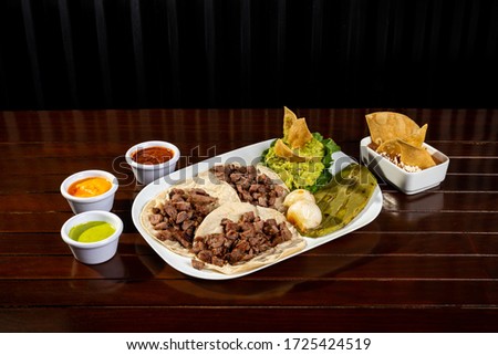beef tacos served with guacamole with grilled tortilla chips and cactus and fried beans and hot sauces on the side