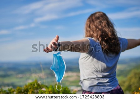 mask in the foreground, held by a girl who has taken it off in the bush Royalty-Free Stock Photo #1725428803