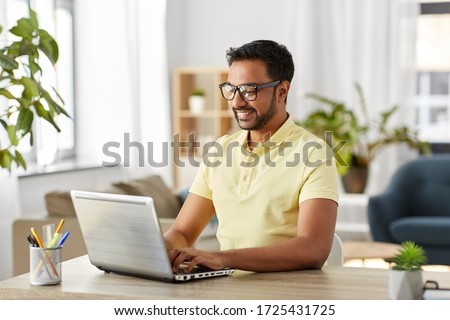 technology, remote job and lifestyle concept - happy indian man in glasses with laptop computer working at home office Royalty-Free Stock Photo #1725431725