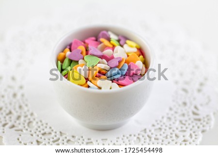 Candies in the form of multi-colored hearts lie in a white plate. Place for text.