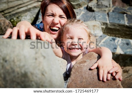 Beautiful mother and pretty small girl on stones in a summer day