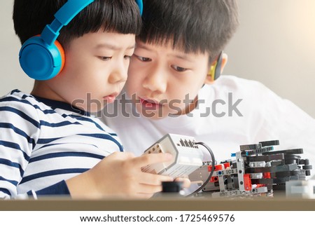Social distancing & Learning activities, Two Asian brothers boys with headphone assemble and test a robot with EV3 components as school project at home due to school closed and Covid-19 pandemic Royalty-Free Stock Photo #1725469576