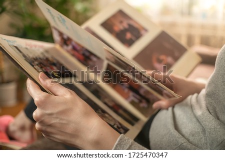 girl in a gray jacket is sitting on the sofa and looking at old photos in a photo album