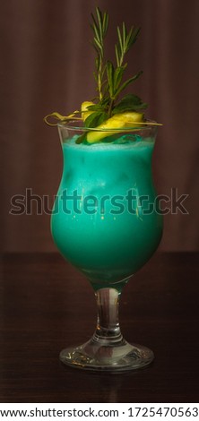 Transparent glass with freshly prepared cocktail Blue Hawaii on a dark brown table