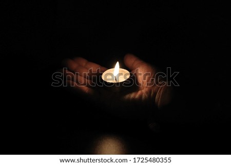 holding burning candle in darkness with noise and grain effect.