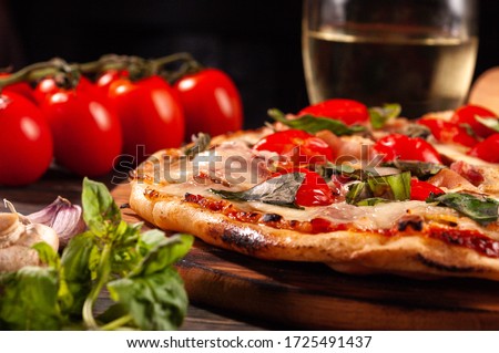Homemade pizza with bacon and mushrooms on a wooden board. Tomatoes and basil.