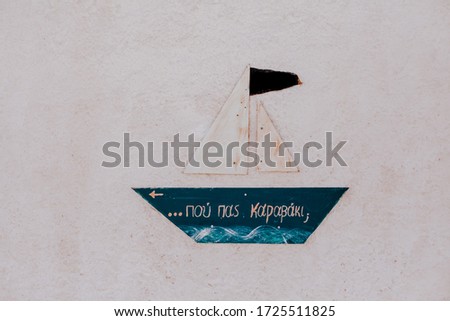 A small blue boat with a text in greek "Where are you going, small boat?"hanging on the white wall 