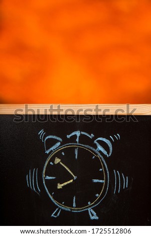 alarm clock drawn in chalk on a blackboard isolated on orange background