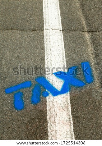 Word Taxi written on the road. White solid single marking line on the road.