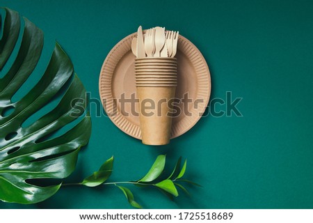Eco friendly craft paper tableware on green background with monstera leaf. Recycling concept. Top view. Copy space. Zero waste theme.