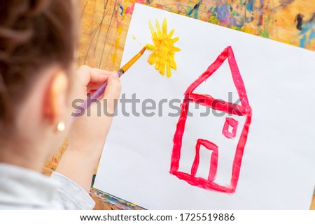 Child is drawing house with watercolors on the easel.