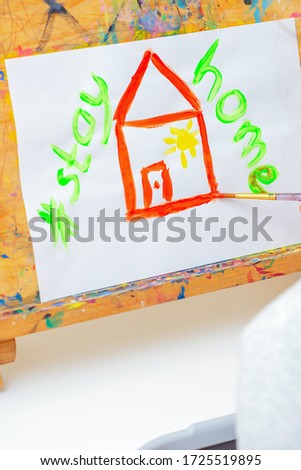 Hand of child drawing red house and words Stay Home with watercolors on the easel at home. Children's creativity concept.