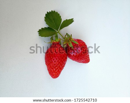 Two ripe strawberries with a leaf in the light background. Summer berries pattern. Positive natural background with place for text. Flat lay. Bio organic food for healthy eating and healthy lifestyle
